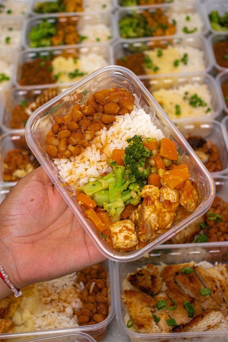 Marmita com arroz, feijão, brócolis e frango sendo mostrada em close