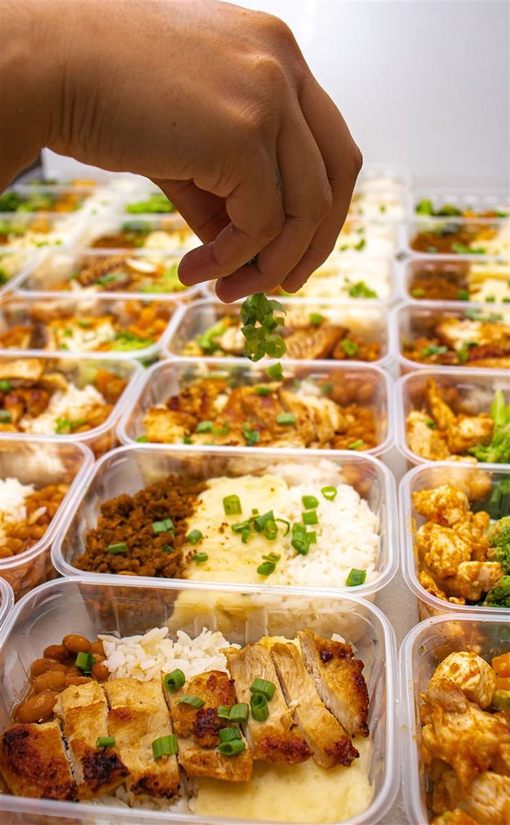 Cebolinha sendo finalizada à mão sobre fileiras de marmitas prontas